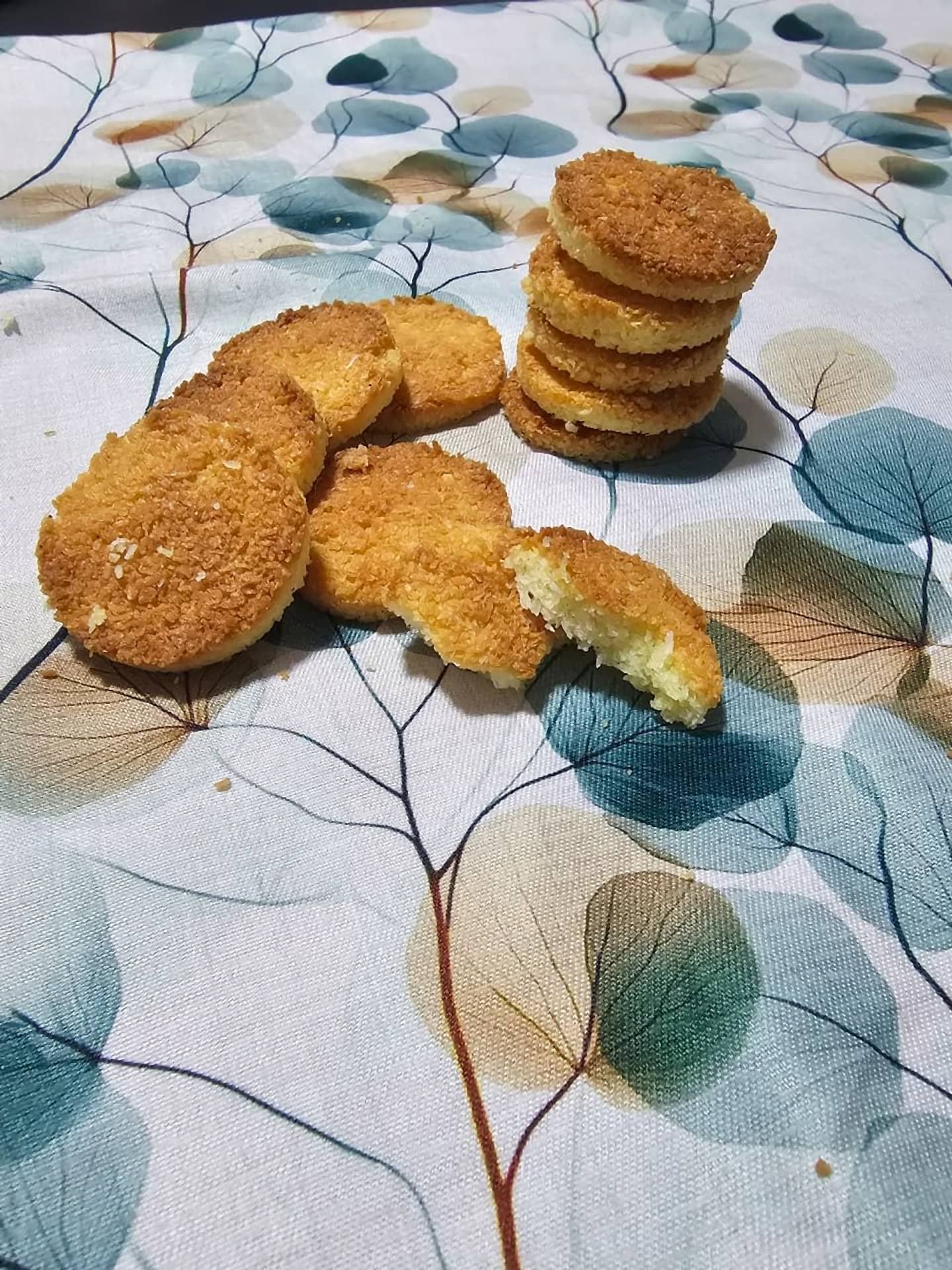 Galletitas de coco doradas apiladas, una mordida muestra el interior tierno